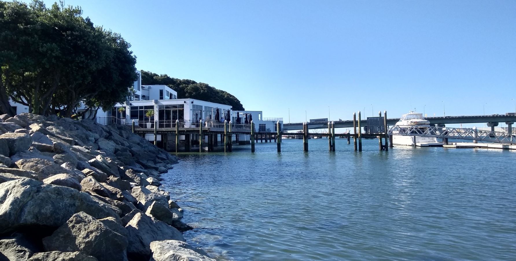 Trinity Wharf jetty on a sunny calm afternoon. A launch is docked at the end on the right. The hotel building is on the left.